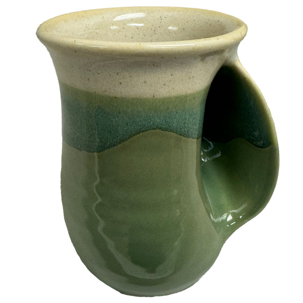 Ceramic mug in earthy green and beige tones with a built-in handwarmer groove, designed for cozy tea sipping inspired by the charm of Charleston Tea Garden.