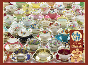A colorful collection of vintage tea cups and saucers with intricate floral and decorative designs, arranged closely together on a wooden surface.