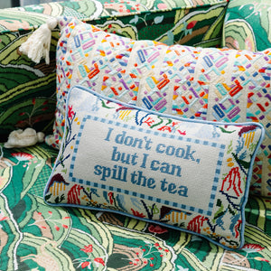 Decorative pillow embroidered with the phrase "I don't cook, but I can spill the tea" resting on a colorful patterned couch in a cozy, inviting setting.