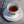 White porcelain tea cup filled with amber tea on a matching saucer with floral design, sitting on a rustic wooden table in natural light.