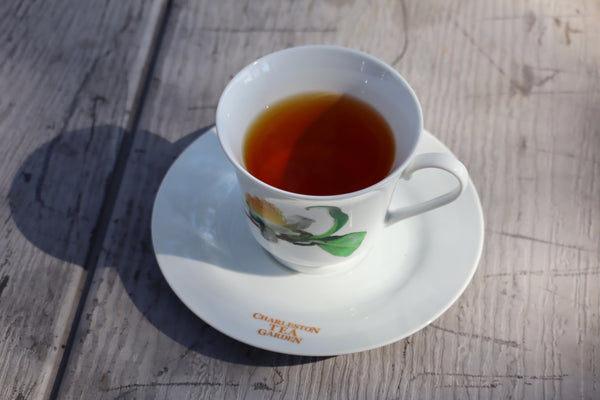 White porcelain tea cup filled with amber tea on a matching saucer with floral design, sitting on a rustic wooden table in natural light.
