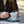 Hands with red nail polish holding a white tea cup and saucer with gold lettering that reads Charleston Tea Garden, set on a wooden table outdoors.