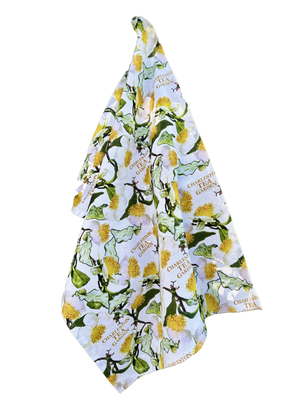 White tea towel featuring a colorful pattern of tea leaves and yellow blossoms with Charleston Tea Garden logos, capturing the charm of American classic tea culture.