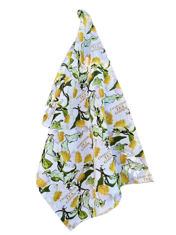 White tea towel featuring a colorful pattern of tea leaves and yellow blossoms with Charleston Tea Garden logos, capturing the charm of American classic tea culture.
