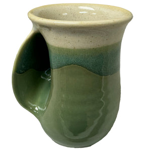 Handcrafted ceramic mug in earthy green and beige tones with a built-in hand warmer, perfect for enjoying American Classic Tea from the Charleston Tea Garden.