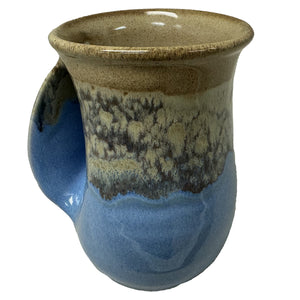A ceramic handwarmer mug with a smooth, curved handle, featuring a sandy beige and ocean blue glaze that evokes a calm beach scene.