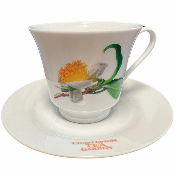 White ceramic tea cup with a floral design and matching saucer featuring the Charleston Tea Garden logo, perfect for enjoying a classic tea experience.