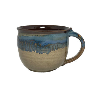 Handcrafted ceramic mug with a smooth beige base and a glossy blue and brown glaze dripping from the rim, perfect for enjoying a cozy latte or tea.
