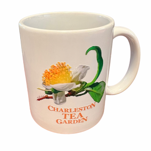 White ceramic mug featuring a detailed illustration of a tea flower with green leaves and warm orange text, perfect for enjoying a cozy tea moment.