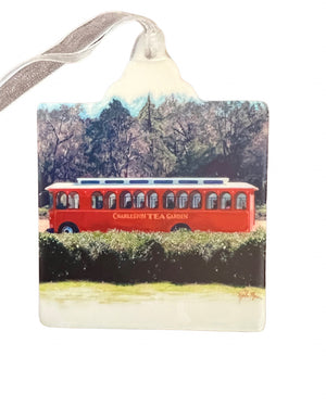 Red trolley bus traveling past lush greenery with trees in the background, capturing a charming scene from the Charleston Tea Garden.