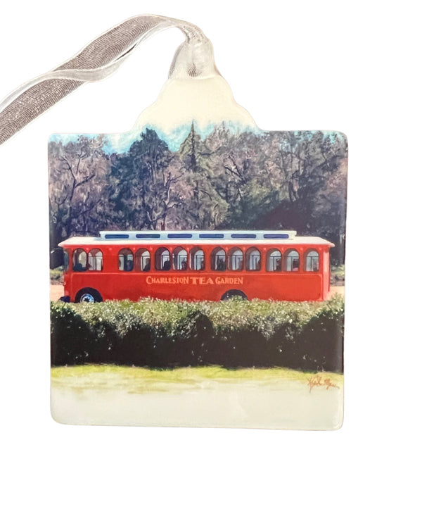 Red trolley bus traveling past lush greenery with trees in the background, capturing a charming scene from the Charleston Tea Garden.