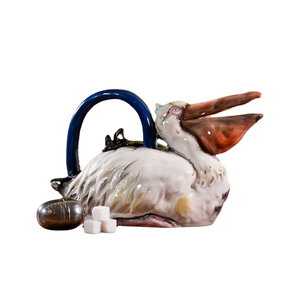 Ceramic teapot shaped like a pelican with a blue handle, accompanied by a tea infuser and sugar cubes, perfect for enjoying a charming tea experience.