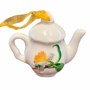 White ceramic teapot ornament with a yellow ribbon hanger, featuring a hand-painted yellow and white flower design on the side.