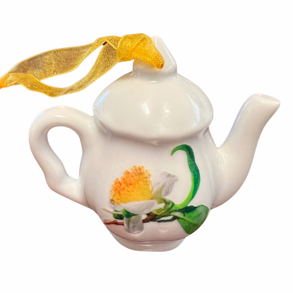 White ceramic teapot ornament with a yellow ribbon hanger, featuring a hand-painted yellow and white flower design on the side.