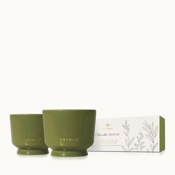 Two olive green ceramic candles labeled Thymes next to a white box with botanical illustrations and citronella grove text.