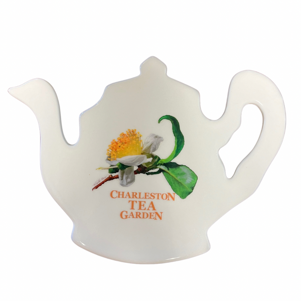 White ceramic tea pot-shaped trivet featuring a delicate illustration of a tea flower and green leaves with “Charleston Tea Garden” printed in orange.