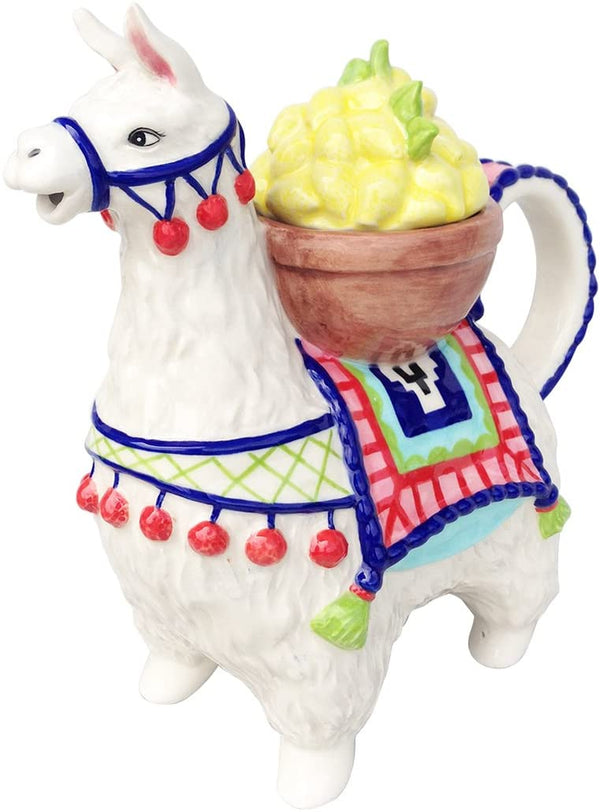 Whimsical ceramic teapot shaped like a white llama adorned with colorful blankets and red pom-pom decorations, featuring a handle and a yellow lemon-shaped lid.
